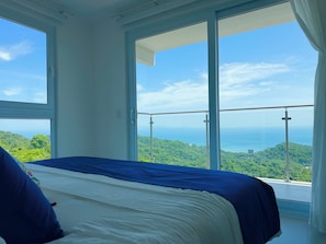 Un dormitorio con una cama grande, vistas a un paisaje montañoso y un balcón con barandilla de cristal.