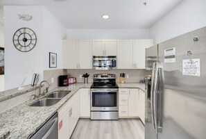 A modern kitchen with granite countertops, stainless steel appliances, and white cabinetry. - 4BR Themed Home W/Resort Pool Near Disney (Kissimmee)