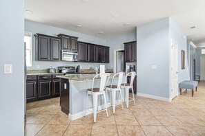 A kitchen with dark cabinets, a granite countertop, a built-in island with bar stools, and a tiled floor. - Lakefront 5BR Family Resort Pool Home Near Disney (Kissimmee)