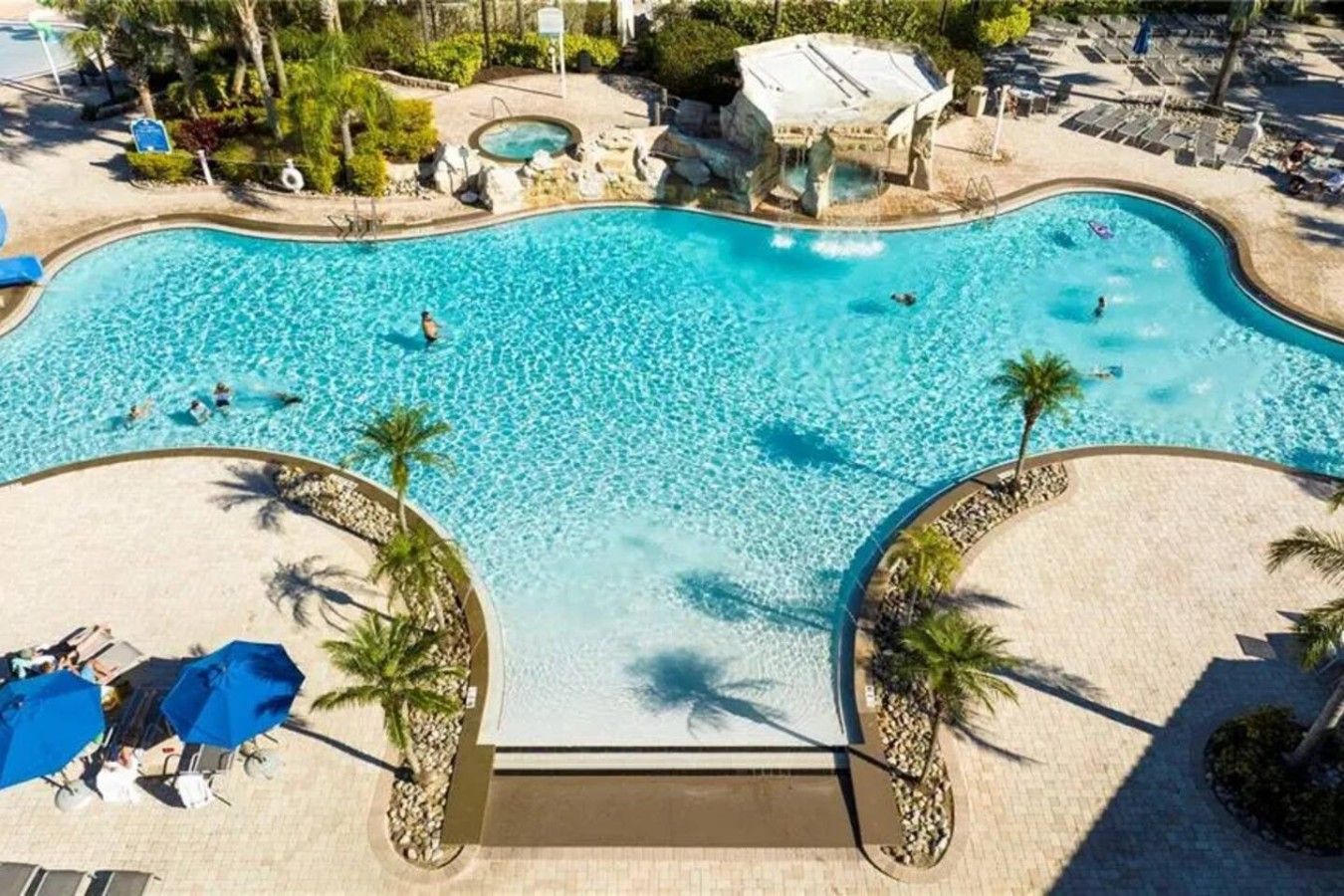 An aerial view of a resort pool with clear water, surrounded by palm trees and lounge chairs.
