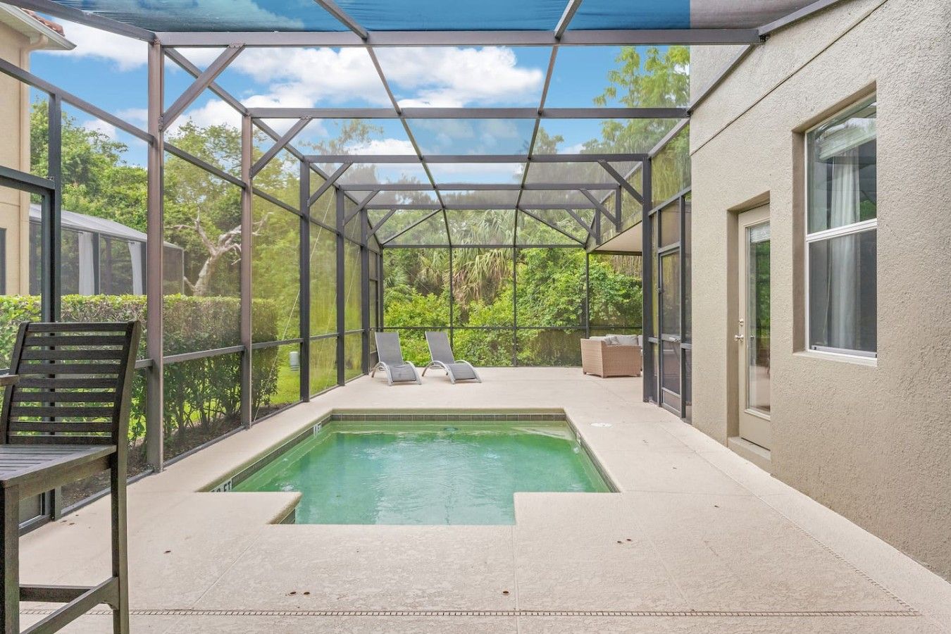 A covered outdoor swimming pool with a metal frame, lounge chairs, and a bench.