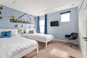 Ein Schlafzimmer mit zwei Betten, einem Schreibtisch, einem Stuhl, einem Fernseher und einem Fenster mit Vorhängen.