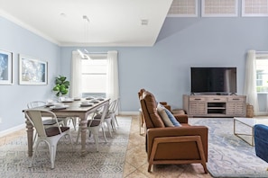 A dining area with a table set for four, a brown leather sofa, a television, and a patterned rug. - Lakefront 5BR Family Resort Pool Home Near Disney (Kissimmee)