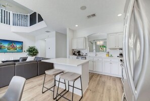 A modern kitchen with white cabinets, a central island with stools, and a staircase leading to an upper level. - Luxury 7BR Lakefront Villa Pool Spa Near Disney (Kissimmee)