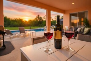 A table with two wine glasses and a bottle of wine, set against a backdrop of a swimming pool and a sunset. - Luxury 7BR Lakefront Villa Pool Spa Near Disney (Kissimmee)