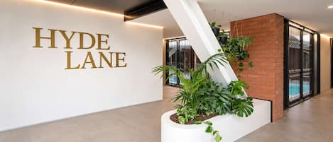 A modern hotel lobby with a white reception desk, a large 'HYDE LANE' sign, and a planter with green plants.