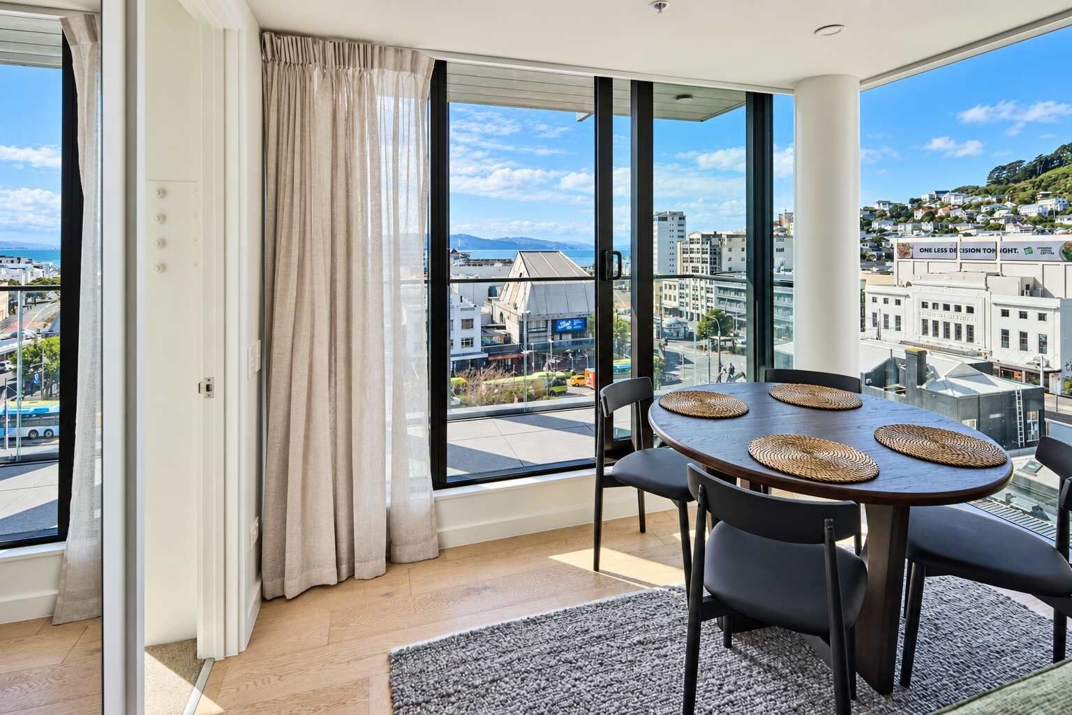A modern room with large windows, a dining table with placemats, and a view of a cityscape.