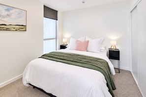 A bedroom with a bed, two bedside tables, a window with a view, and a painting on the wall. - Central Te Aro 2BR with Balcony & Indoor Pool (Wellington)