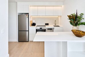 A modern kitchen with white cabinetry, stainless steel appliances, and a wooden bowl on the island. - Central Te Aro 2BR with Balcony & Indoor Pool (Wellington)