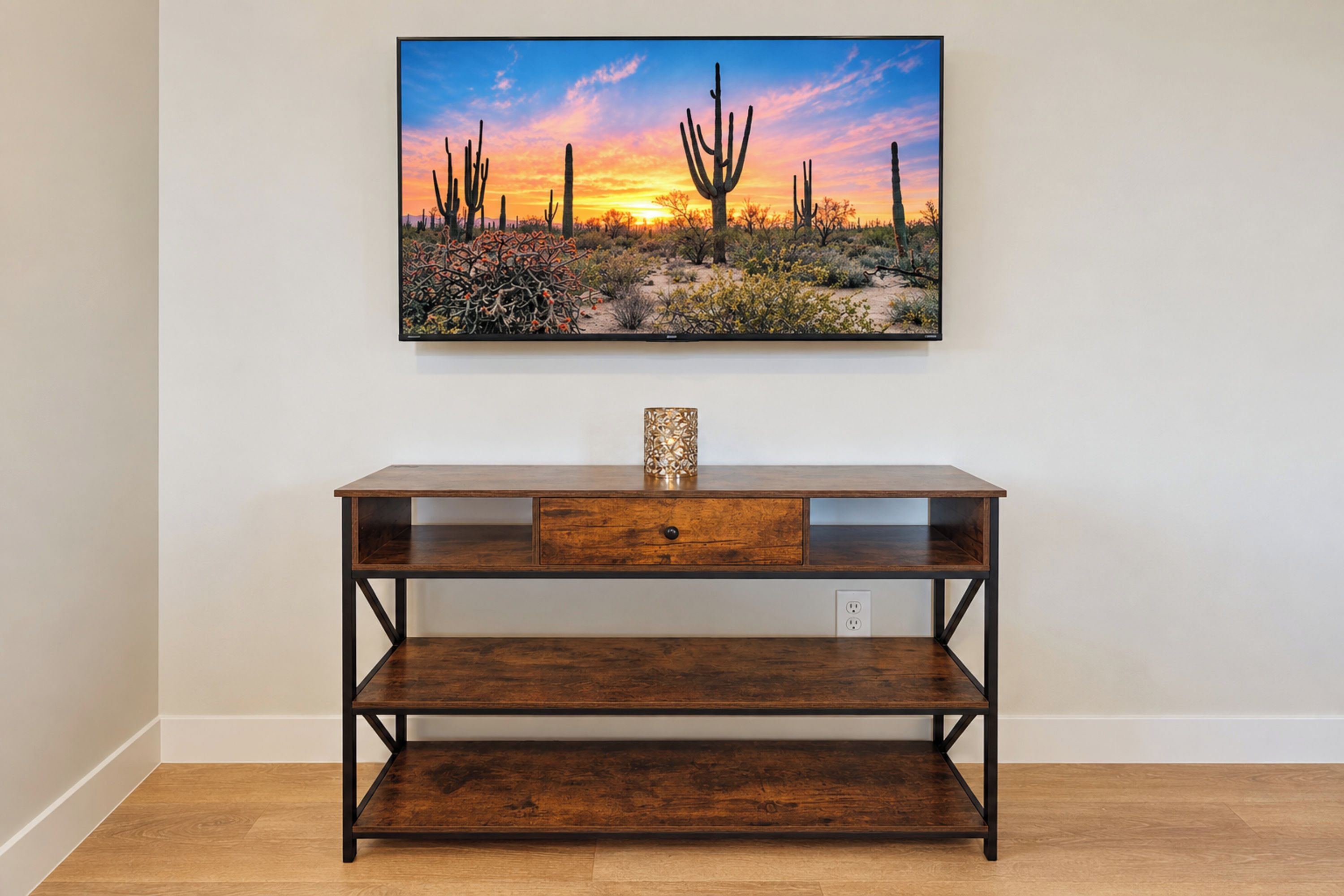 A wooden console table with a drawer and shelves, positioned in front of a wall-mounted painting of a desert landscape.