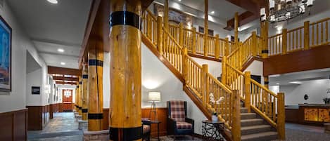 A grand staircase with wooden railings, a stone floor, and a chandelier.