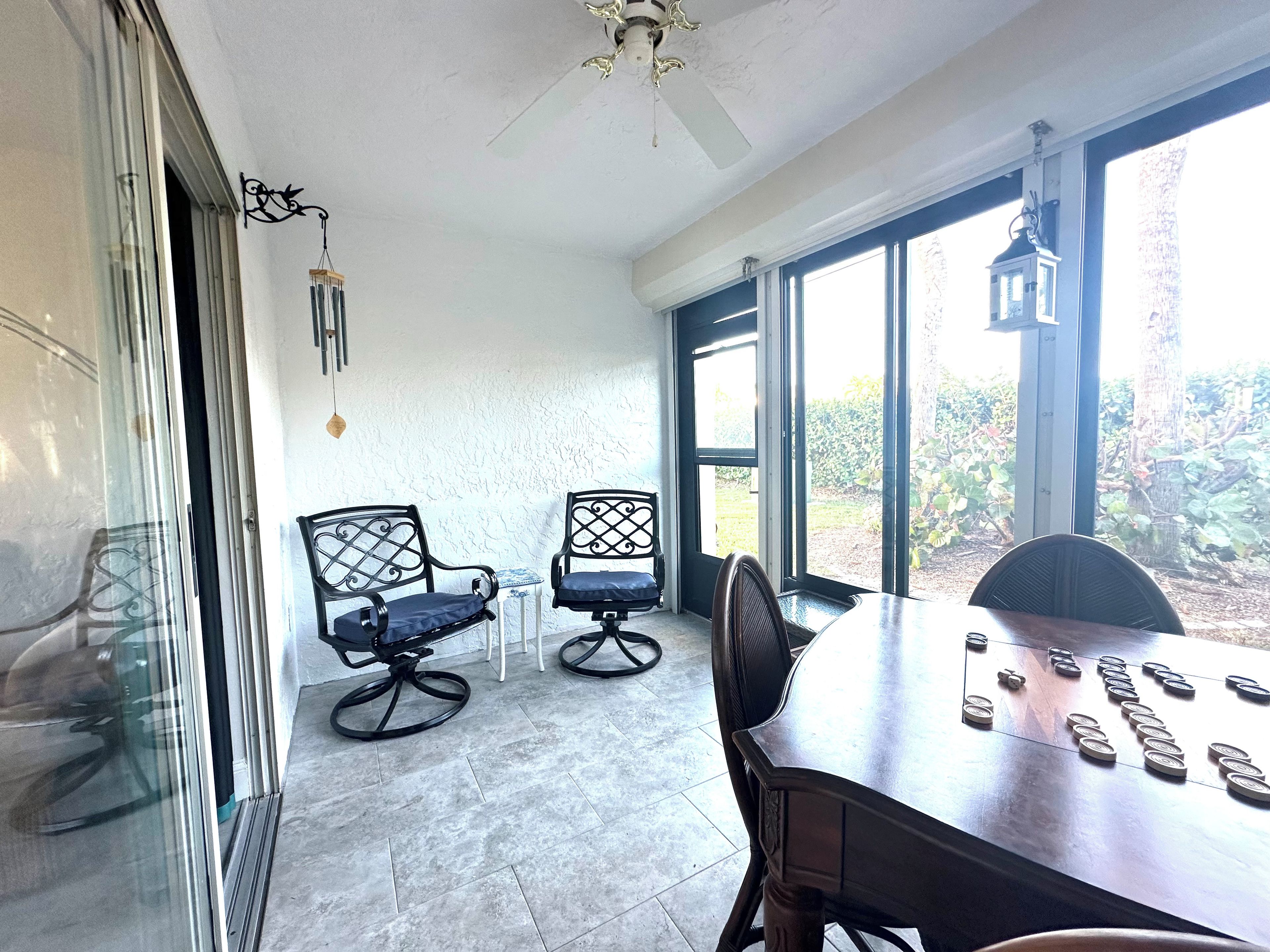 A room with a dining table, two chairs, a ceiling fan, and a view through large windows.