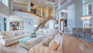 A spacious living area with a high ceiling, a staircase leading to an upper level, and a dining area with chairs. - Welcome to Palma Verde, a refined waterfront retreat where comfort, craftsmanshi (Marco Island)