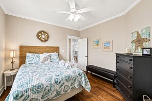 Ein Schlafzimmer mit einem Bett, einem Nachttisch, einer Kommode, einer Bank, einer Tür und einem Deckenventilator.