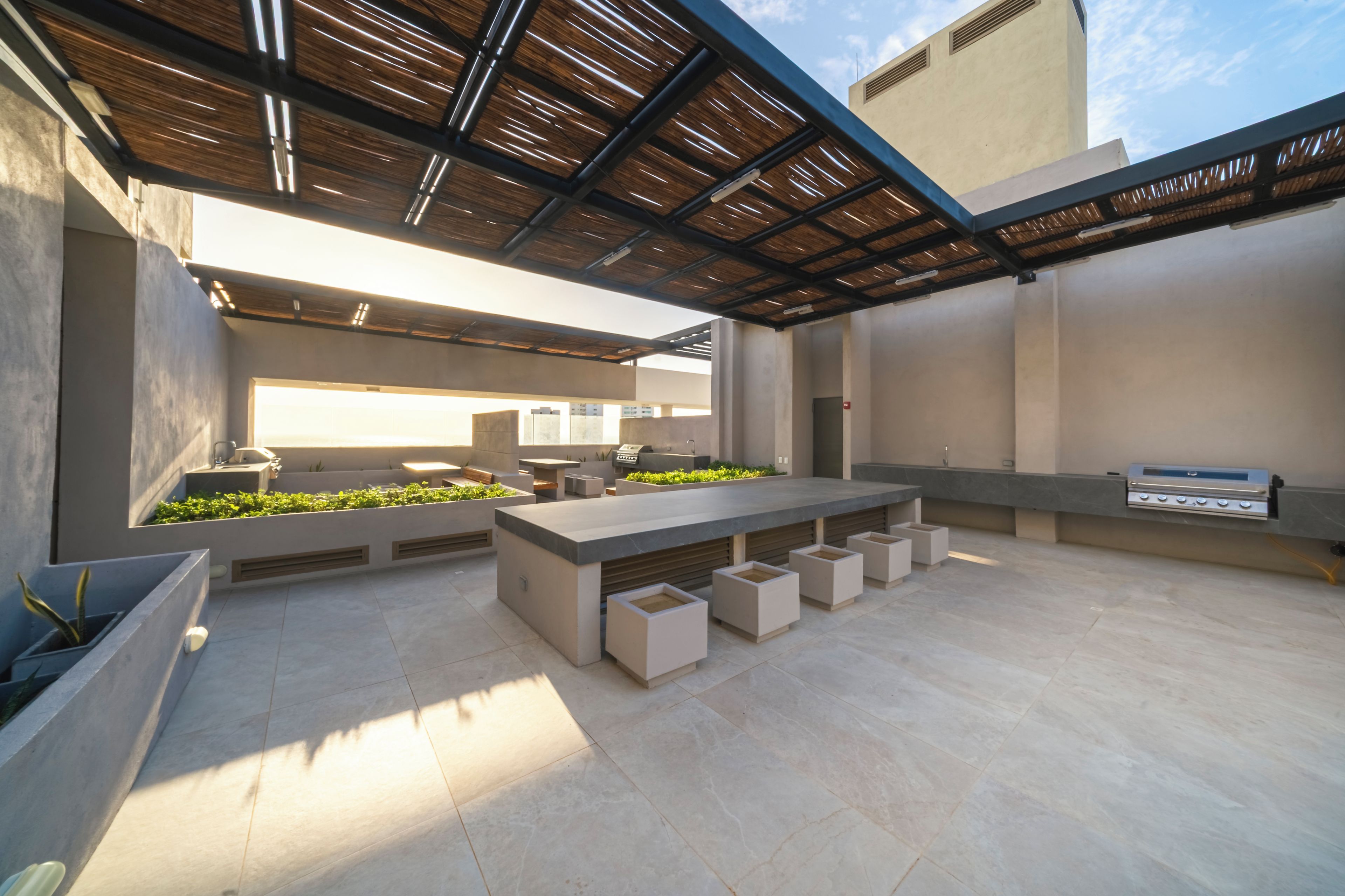An outdoor patio area with a long table, planters with greenery, and a grill station.