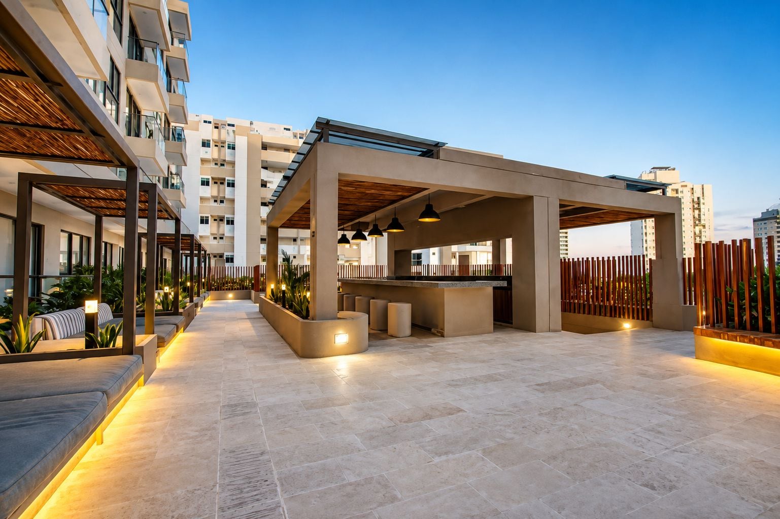 A modern outdoor lounge area with seating and a bar, surrounded by high-rise buildings.