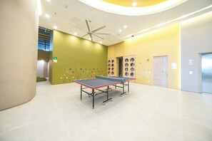 Zona interior àmplia amb taula de ping-pong, ventilador de sostre i paret d'escalada amb agafades de colors.