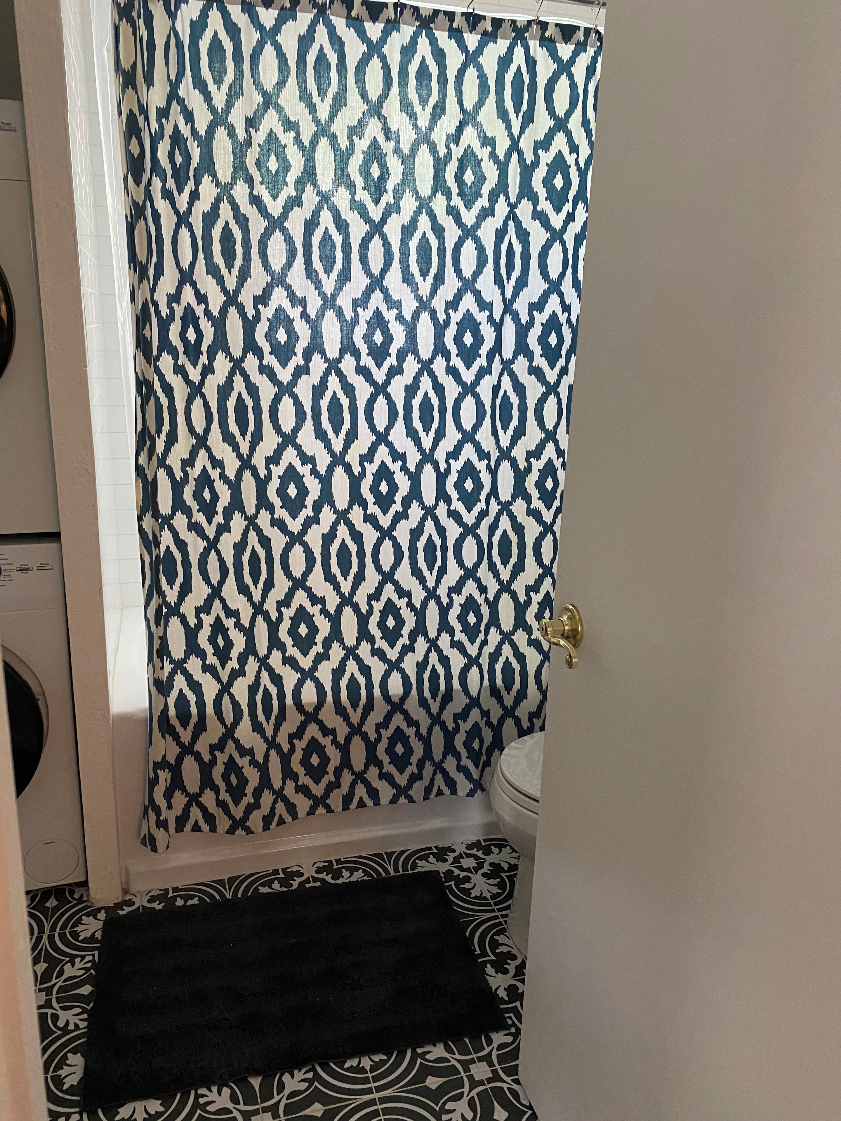 A bathroom with a patterned shower curtain, a toilet, and a black towel on the floor.