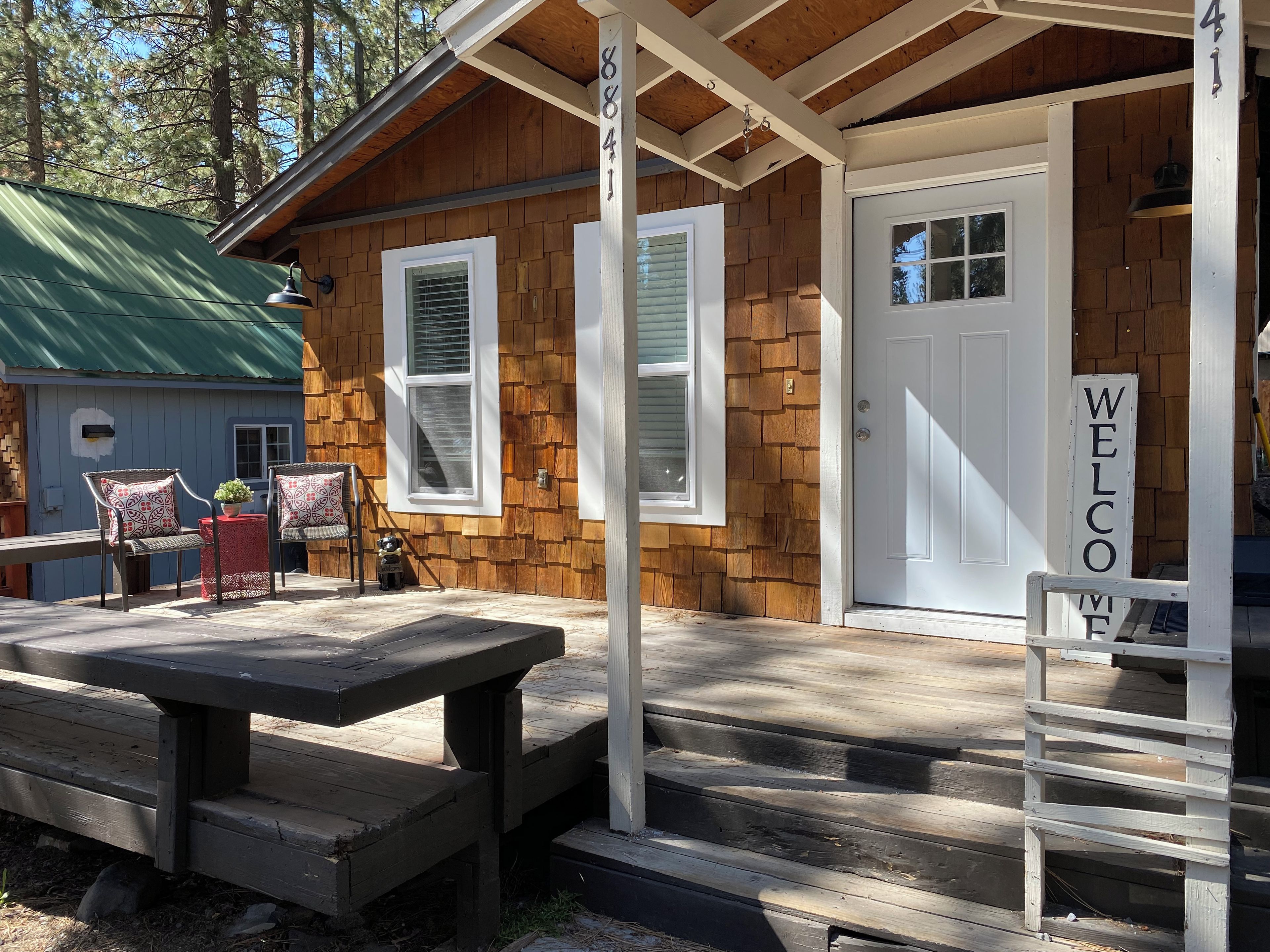 Une cabane en bois avec une véranda, une pancarte de bienvenue et une table de pique-nique.
