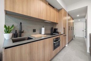 Eine moderne Küche mit Holdekor-Schränken, einer Edelstahl-Spüle, einem schwarzen Wasserhahn, einer Arbeitsplatte mit Schneidebrett, einer Kaffeemaschine und einem Bosch-Ofen.
