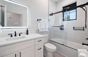A modern bathroom with a large mirror, white vanity, and a glass-enclosed shower.