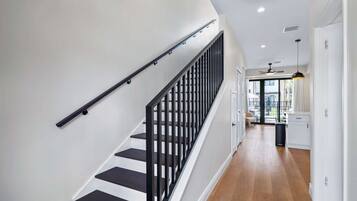 A staircase with black railings leading to a room with a ceiling fan and a view of an outdoor area.