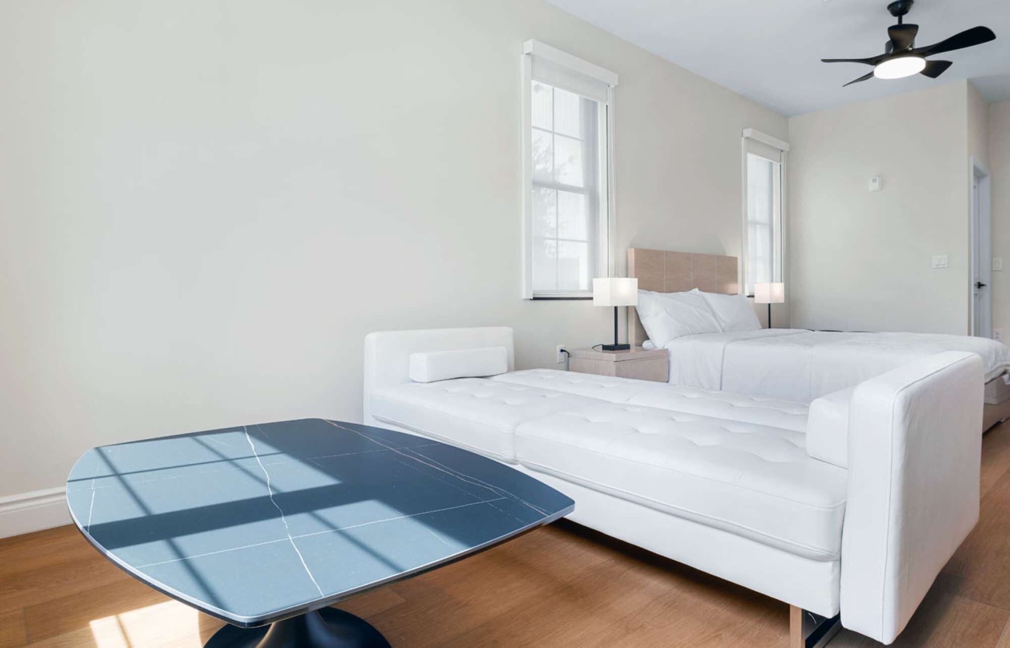 Une chambre d’hôtel avec un lit, une table de chevet, une lampe, un ventilateur de plafond et une petite table.
