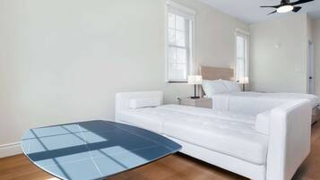 A hotel room with a bed, a bedside table, a lamp, a ceiling fan, and a small table.