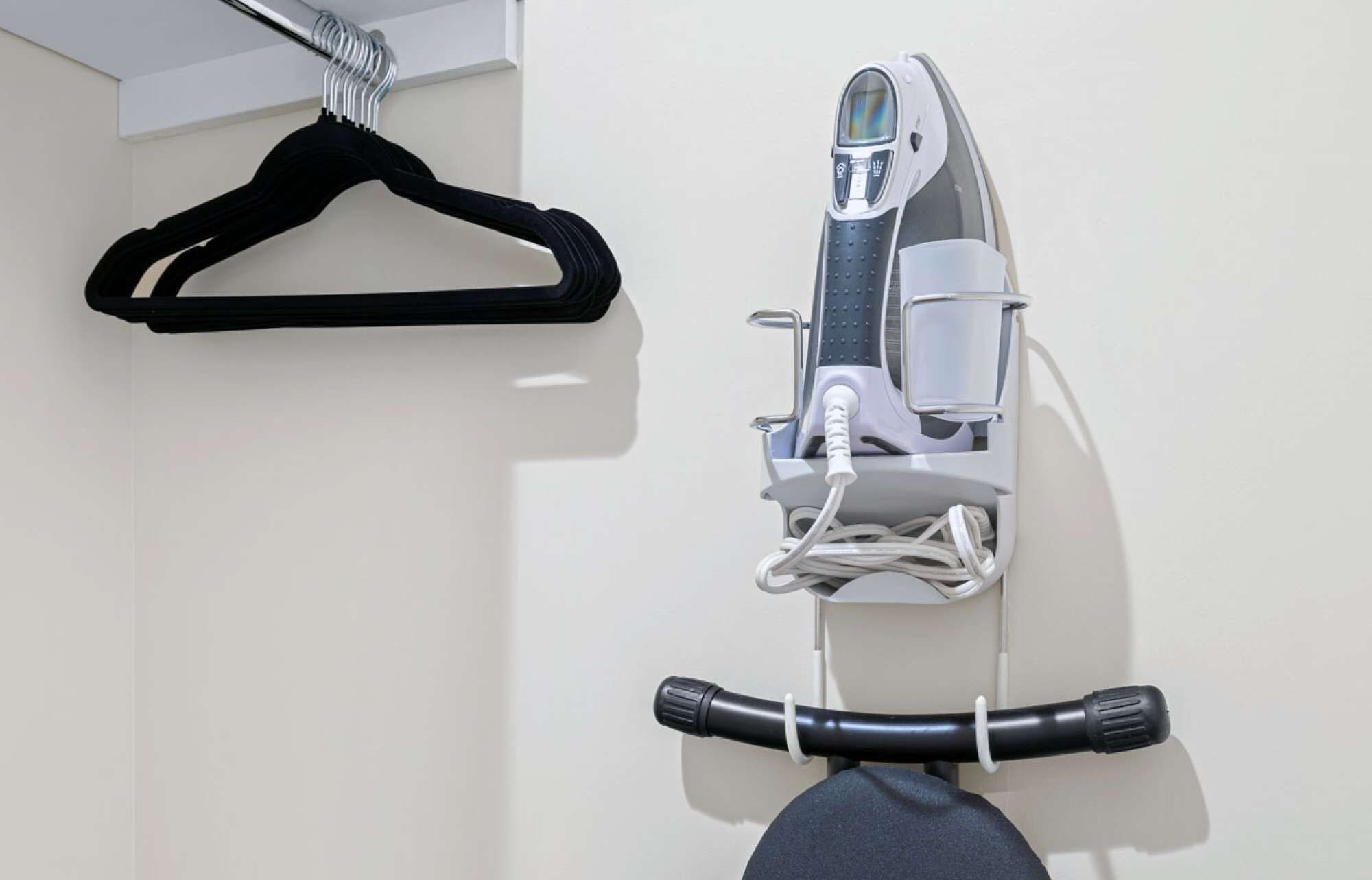 A wall-mounted ironing board with an iron and a hanging black hanger.
