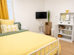 A hotel room with a bed, a TV, a small wooden cabinet, and a white shelf with kitchen items. -     Charming Island Studio Relax & Unwind in Anguilla (The Valley)