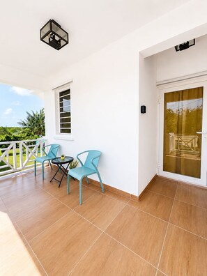 A balcony with two chairs and a table, a window, and a door with a glass panel. -     Charming Island Studio Relax & Unwind in Anguilla (The Valley)