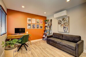 A living room with a television, a sofa, a desk, and a bookshelf. - Hot Tub • Greenbelt• Fireplace • Telescope • Pets (Garden City)