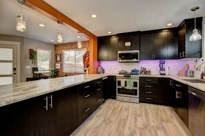 A modern kitchen with dark cabinets, a large island, and pendant lighting. - Hot Tub • Greenbelt• Fireplace • Telescope • Pets (Garden City)