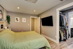 A bedroom with a bed, a TV mounted on the wall, a closet with clothes, and a door leading to another room. - Hot Tub • Greenbelt• Fireplace • Telescope • Pets (Garden City)