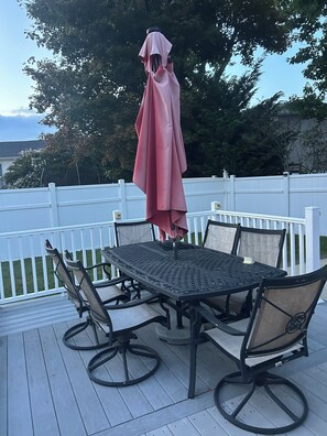 An outdoor patio with a table and chairs, a covered umbrella, and a white fence.