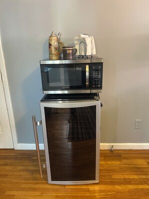 A microwave oven with a built-in oven on a wooden floor, a white wall, and a power outlet.
