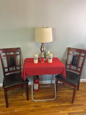A dining table with a red tablecloth, two chairs, a lamp, and two mugs with a design.