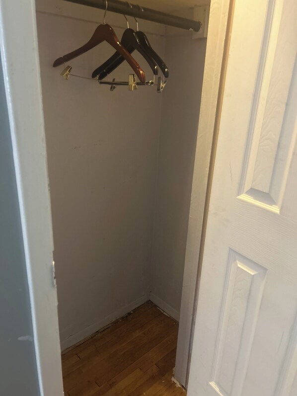 A corner of a room with a wooden floor, a white door, and a clothes rack with hangers.