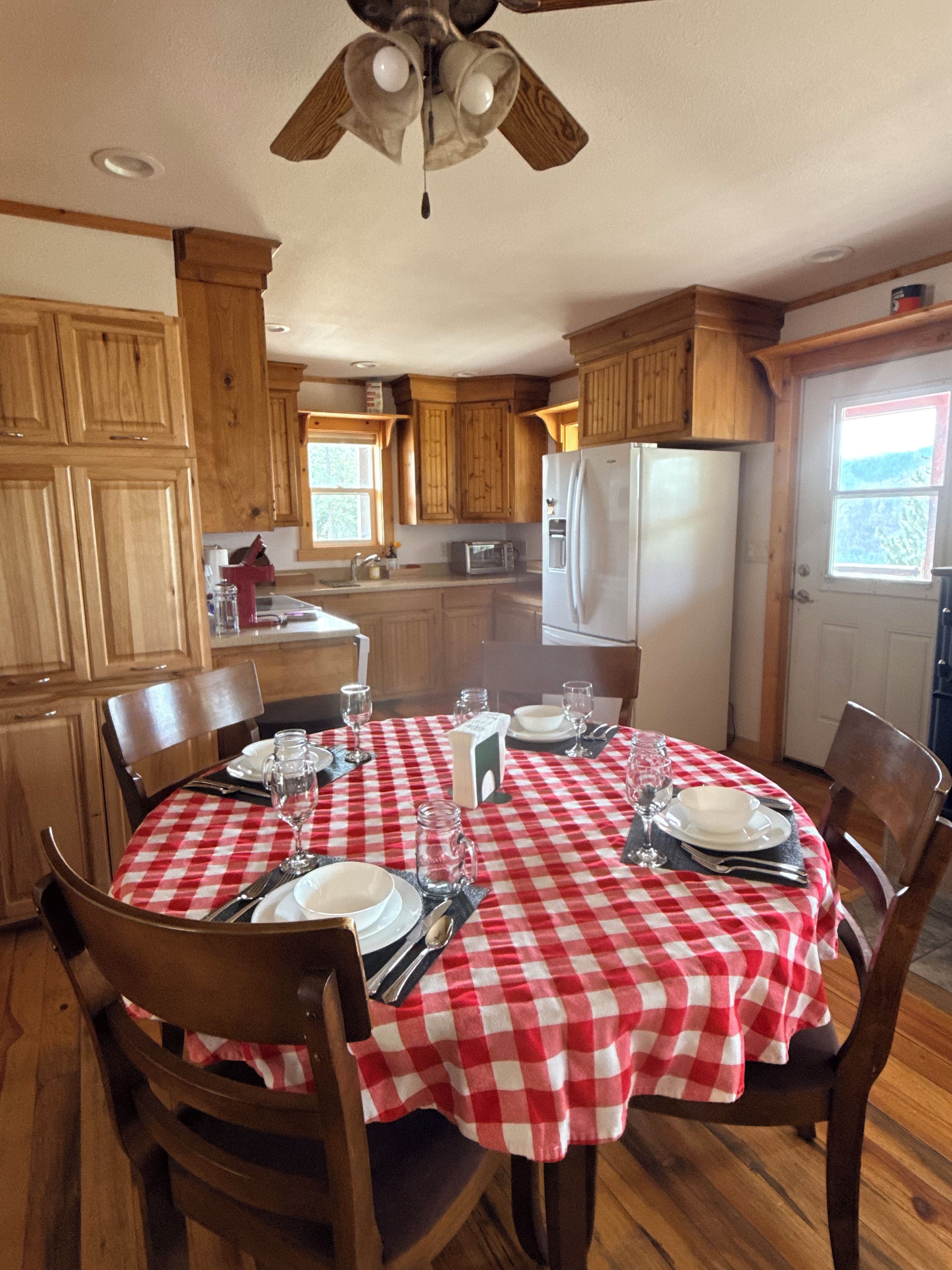 A dining area with a red and white checkered tablecloth, wooden chairs, and a ceiling fan.