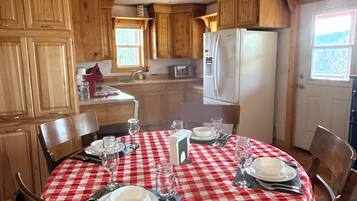 A dining area with a red and white checkered tablecloth, wooden chairs, and a ceiling fan.