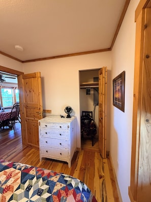 A room with a wooden dresser, a fan, and a quilt on the bed.