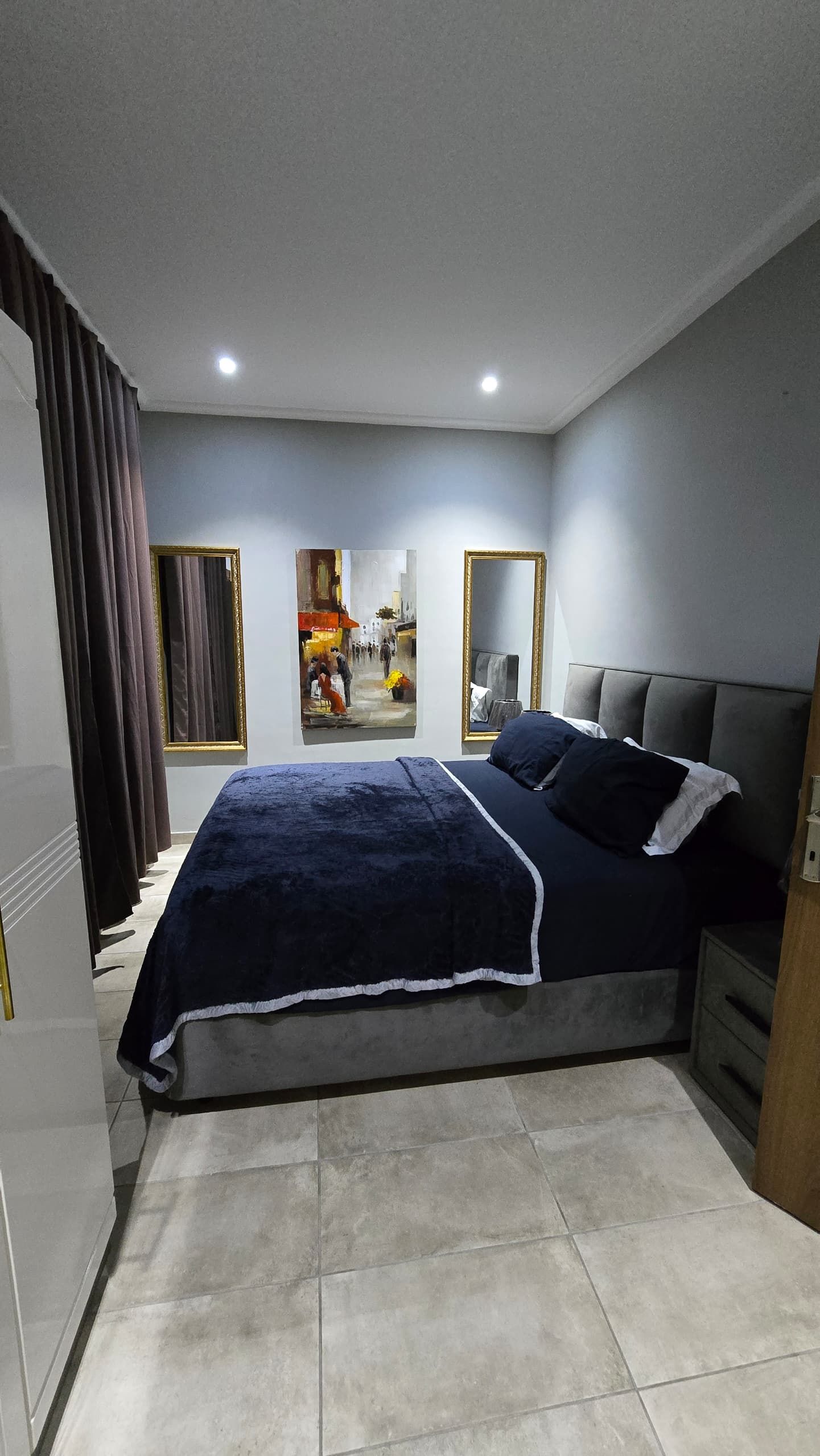 Une chambre à coucher avec un lit, des rideaux, un tableau et un miroir.