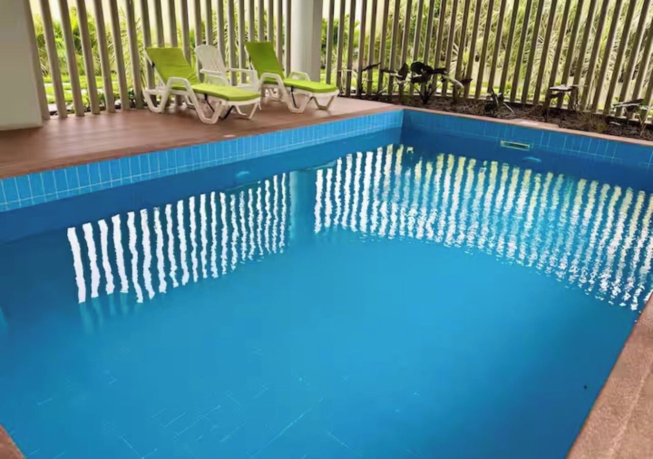Une piscine dont le bord est recouvert de carrelage, entourée d’une terrasse en bois et de chaises longues vertes.