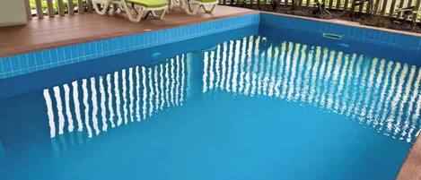 A swimming pool with a tiled edge, surrounded by a wooden deck and green lounge chairs.