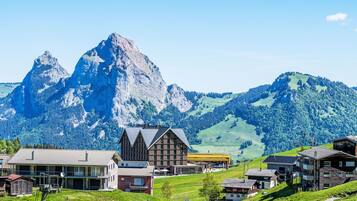 Ein Bergdorf mit traditionellen Holzhäusern, einem modernen Gebäude und einem markanten Berggipfel im Hintergrund.