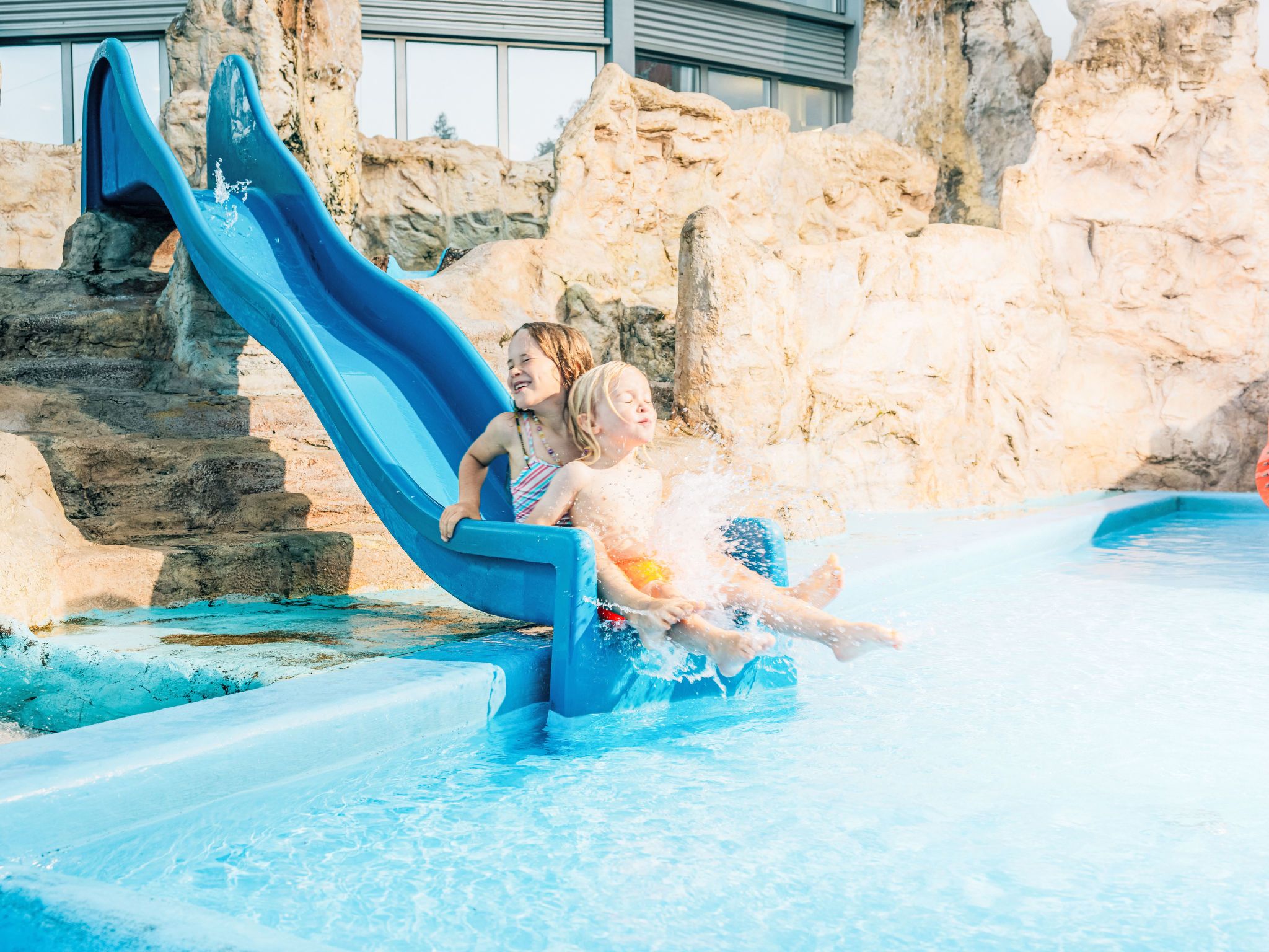 Eine Wasserrutsche an einem Pool mit steinernen Wänden und blauem, klarem Wasser.