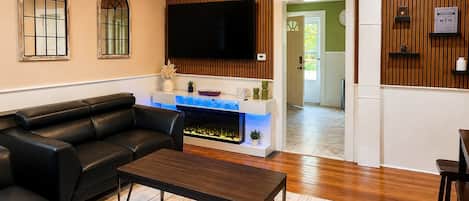 Un salon avec un canapé en cuir noir, une table basse en bois et une cheminée agrémentée d’une touche de bleu.