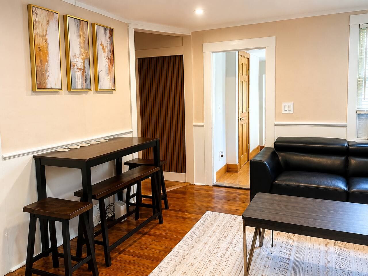 Una sala de estar con una mesa de madera oscura, un sofá de cuero negro y una alfombra estampada.