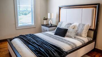 Un dormitorio moderno con cama, mesita de noche, lámpara y ventana.