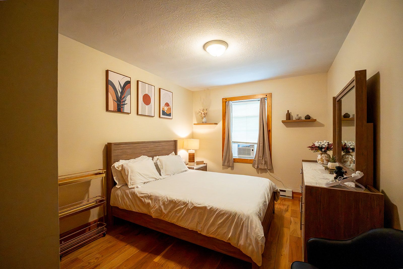 A hotel room with a bed, a nightstand, a mirror, and artwork on the wall.